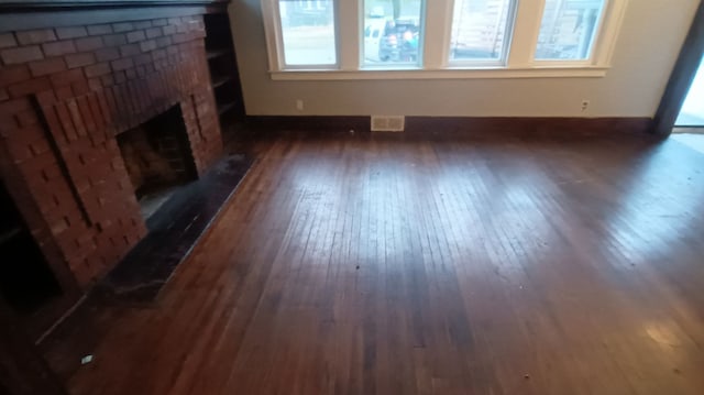 unfurnished living room featuring a brick fireplace and dark wood-type flooring