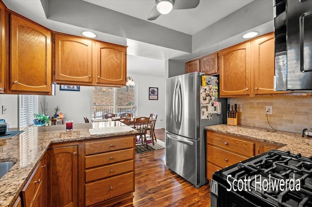 kitchen with light stone counters, dark wood-type flooring, stainless steel fridge, and kitchen peninsula