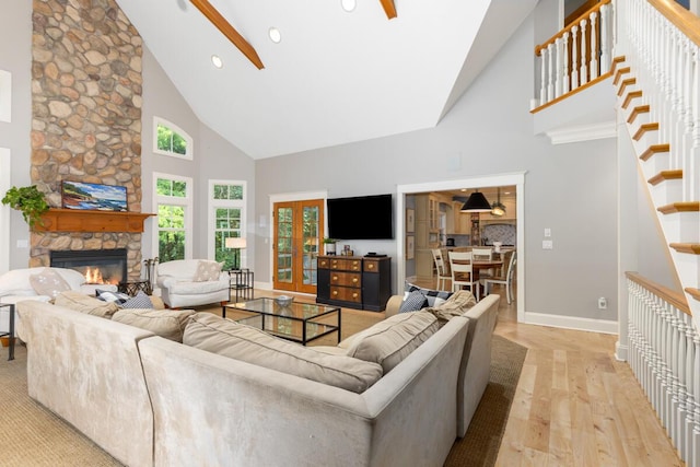 living room featuring a stone fireplace, high vaulted ceiling, ceiling fan, and light wood-type flooring