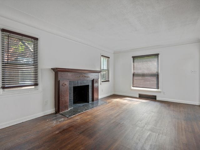 unfurnished living room with a tiled fireplace and dark wood-type flooring