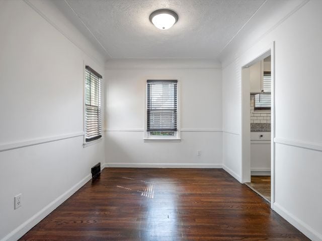 empty room featuring dark wood-type flooring, a healthy amount of sunlight, and a textured ceiling