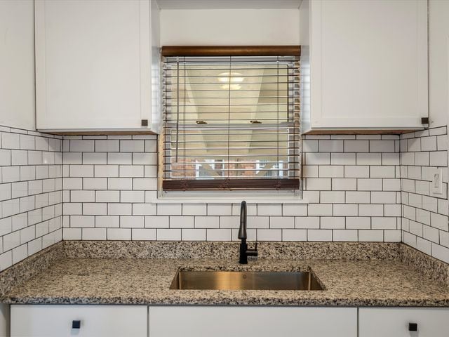 kitchen featuring stone counters, sink, white cabinets, and backsplash