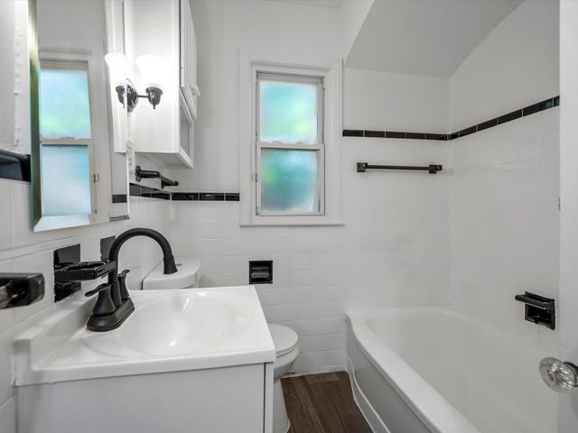 bathroom featuring toilet, wood-type flooring, tile walls, vanity, and a bathing tub