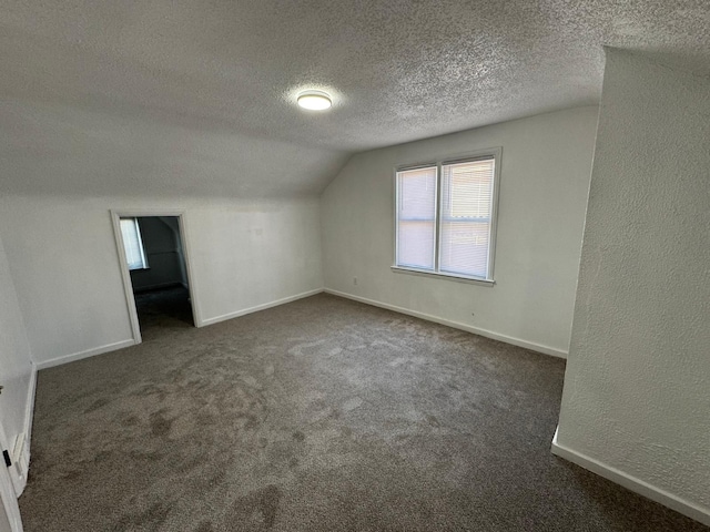 additional living space with vaulted ceiling, dark carpet, and a textured ceiling