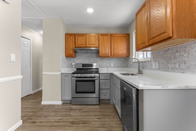 kitchen with sink, backsplash, hardwood / wood-style floors, stainless steel appliances, and light stone counters