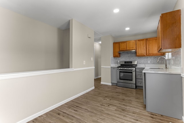 kitchen with tasteful backsplash, stainless steel gas range, sink, and light hardwood / wood-style flooring