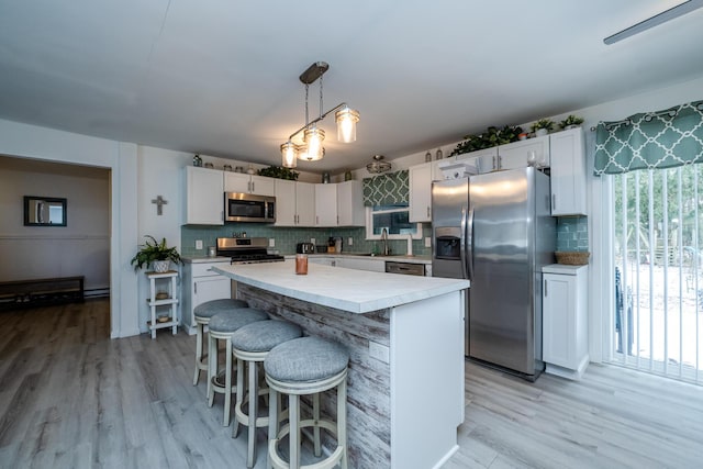 kitchen featuring sink, white cabinetry, decorative light fixtures, appliances with stainless steel finishes, and a kitchen island