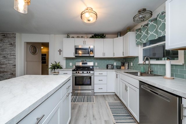 kitchen featuring appliances with stainless steel finishes, tasteful backsplash, white cabinetry, sink, and light hardwood / wood-style floors