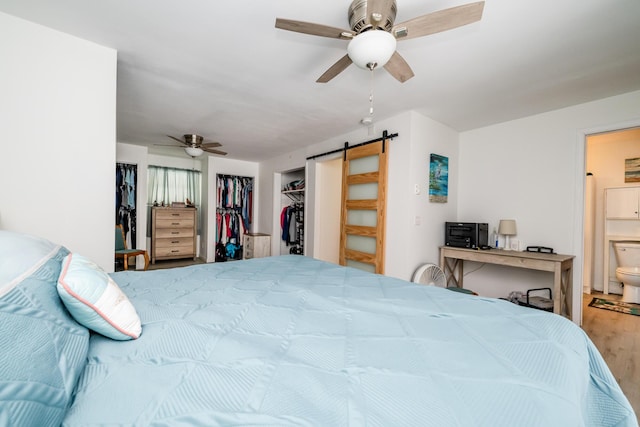 bedroom featuring hardwood / wood-style flooring, ceiling fan, ensuite bathroom, a spacious closet, and a barn door