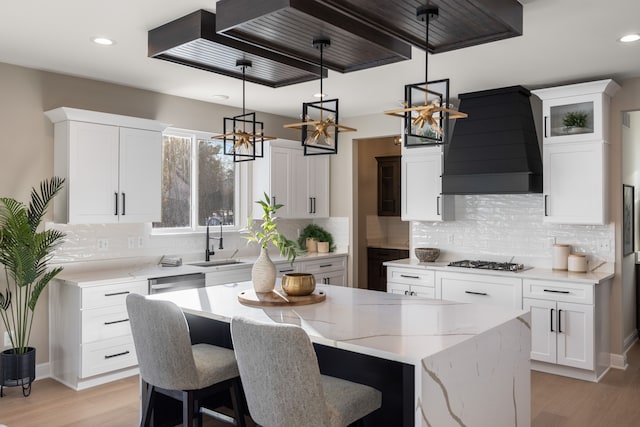 kitchen with white cabinets, a kitchen island, decorative light fixtures, custom exhaust hood, and a sink