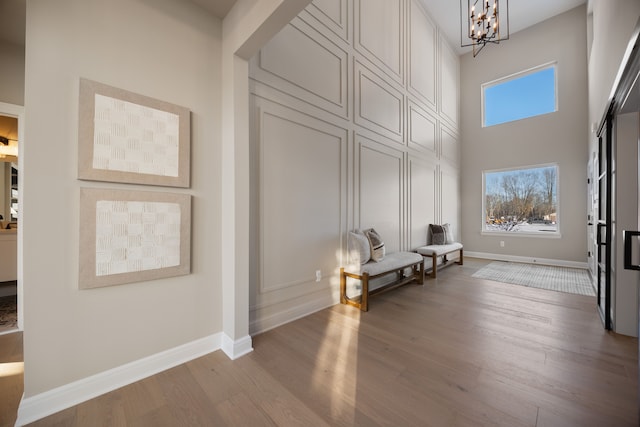 living area with a towering ceiling, baseboards, a chandelier, and wood finished floors