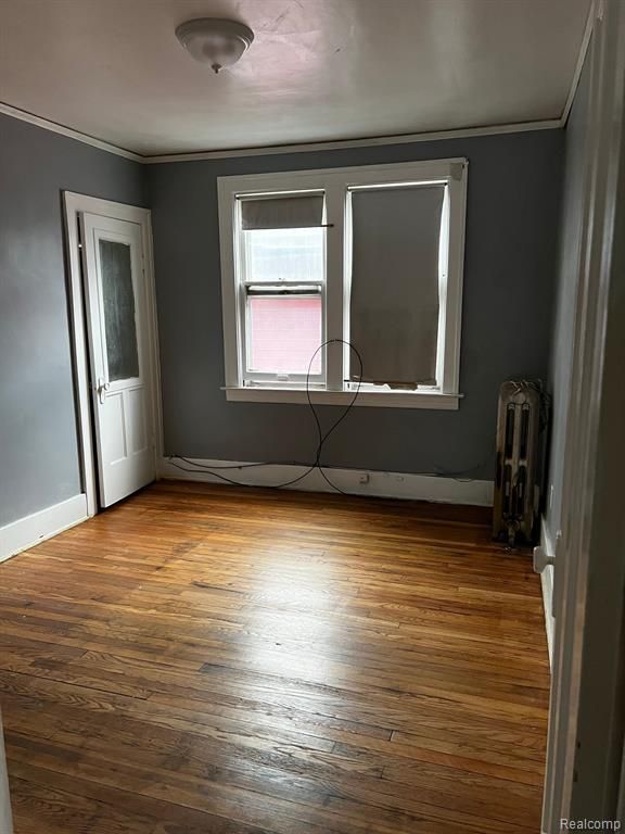 empty room with hardwood / wood-style floors, radiator heating unit, and ornamental molding