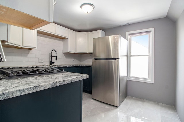 kitchen with stainless steel fridge, white cabinetry, stove, light stone counters, and tasteful backsplash