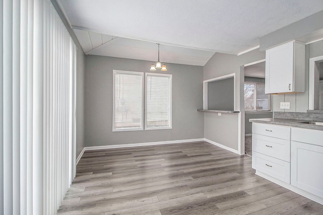 unfurnished dining area featuring an inviting chandelier, sink, vaulted ceiling, and light hardwood / wood-style floors