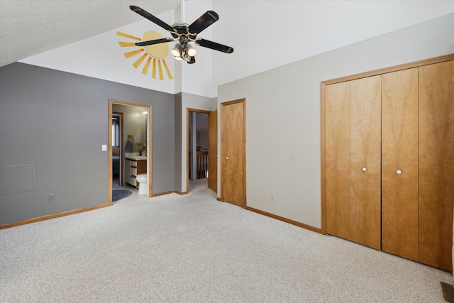 unfurnished bedroom with vaulted ceiling, ensuite bathroom, ceiling fan, light carpet, and two closets