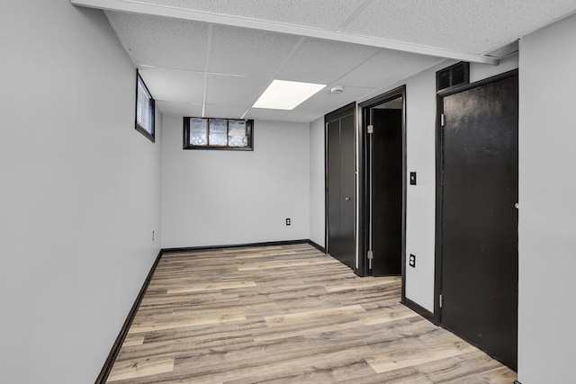 basement featuring a paneled ceiling and light wood-type flooring