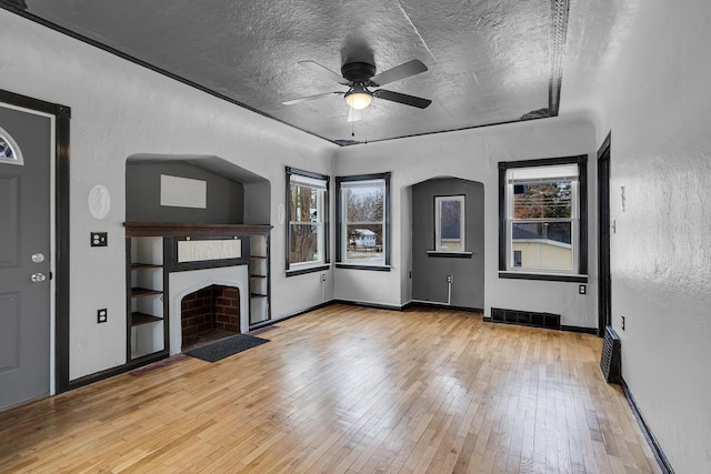 unfurnished living room featuring a healthy amount of sunlight, ceiling fan, a textured ceiling, and light wood-type flooring