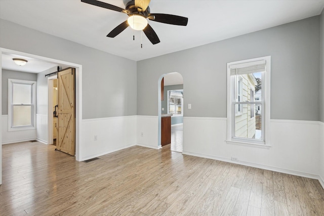 spare room featuring ceiling fan, a barn door, and light hardwood / wood-style flooring