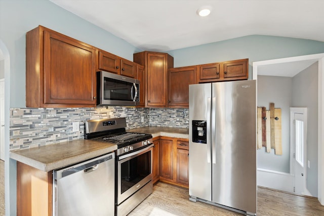 kitchen featuring tasteful backsplash, lofted ceiling, appliances with stainless steel finishes, and light hardwood / wood-style flooring