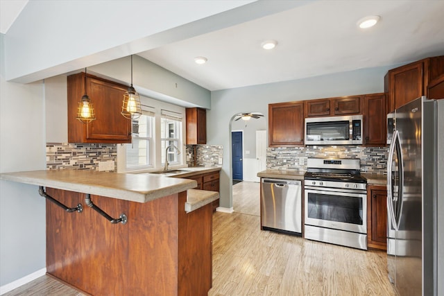 kitchen featuring sink, appliances with stainless steel finishes, hanging light fixtures, kitchen peninsula, and light wood-type flooring