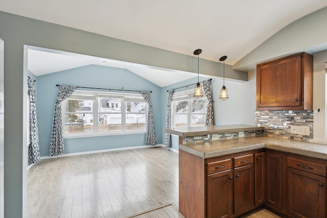 kitchen featuring vaulted ceiling, decorative light fixtures, backsplash, and kitchen peninsula