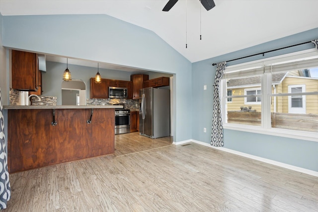 kitchen featuring pendant lighting, stainless steel appliances, kitchen peninsula, and light hardwood / wood-style floors