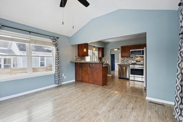 kitchen featuring appliances with stainless steel finishes, pendant lighting, wood-type flooring, a kitchen bar, and kitchen peninsula