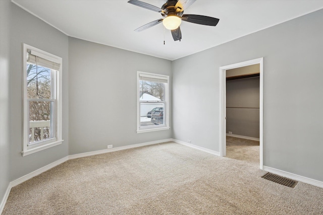 unfurnished bedroom with multiple windows, a walk in closet, light colored carpet, and ceiling fan