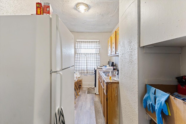 kitchen featuring sink, a textured ceiling, white fridge, and light wood-type flooring