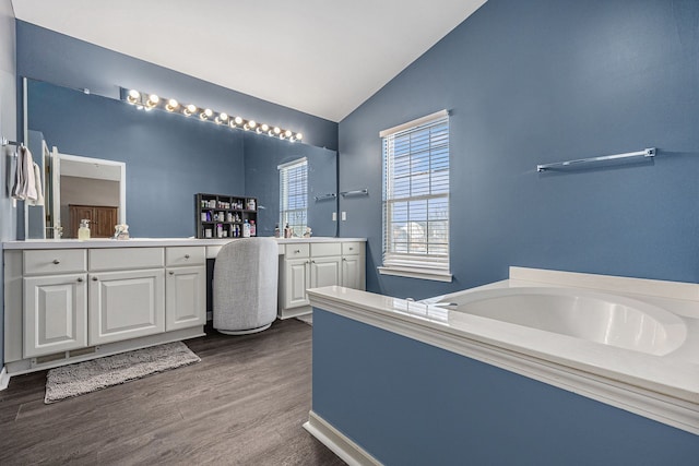 bathroom featuring two vanities, vaulted ceiling, a garden tub, and wood finished floors