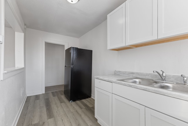 kitchen with sink, light hardwood / wood-style floors, white cabinets, and black fridge