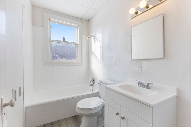 full bathroom featuring toilet, tiled shower / bath, wood-type flooring, vanity, and a drop ceiling