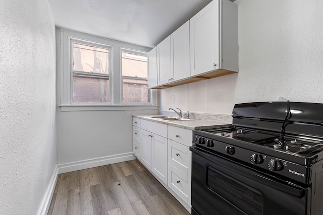 kitchen featuring sink, black range with gas stovetop, white cabinets, and light wood-type flooring