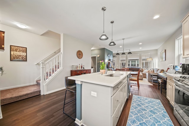 kitchen featuring a center island with sink, hanging light fixtures, stainless steel stove, sink, and a kitchen breakfast bar