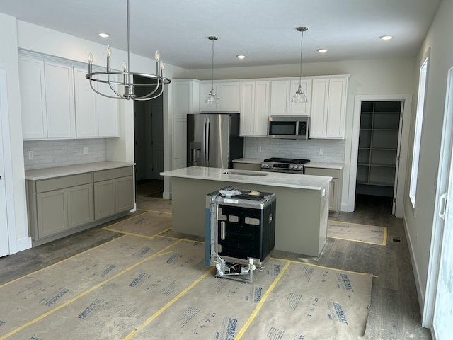 kitchen with a center island with sink, white cabinetry, decorative light fixtures, stainless steel appliances, and dark hardwood / wood-style flooring