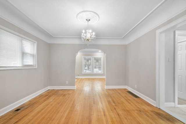 empty room featuring an inviting chandelier, crown molding, and wood-type flooring