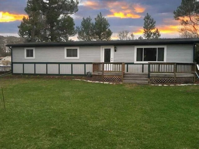 back house at dusk with a deck and a lawn