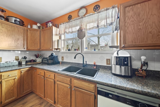 kitchen with dishwasher, sink, dark stone counters, decorative backsplash, and light hardwood / wood-style flooring