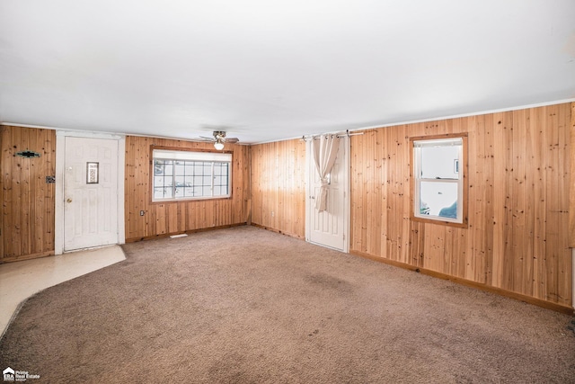 carpeted empty room featuring ceiling fan and wood walls