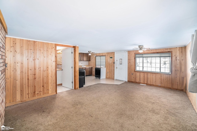 unfurnished living room with ceiling fan, light colored carpet, and wooden walls