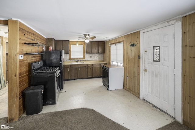 kitchen with sink, ceiling fan, dark brown cabinets, black appliances, and wood walls