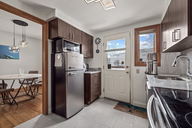 kitchen with pendant lighting, sink, appliances with stainless steel finishes, dark brown cabinetry, and decorative backsplash