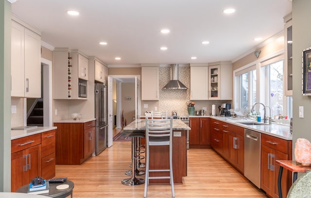 kitchen with sink, white cabinets, a center island, stainless steel appliances, and wall chimney range hood