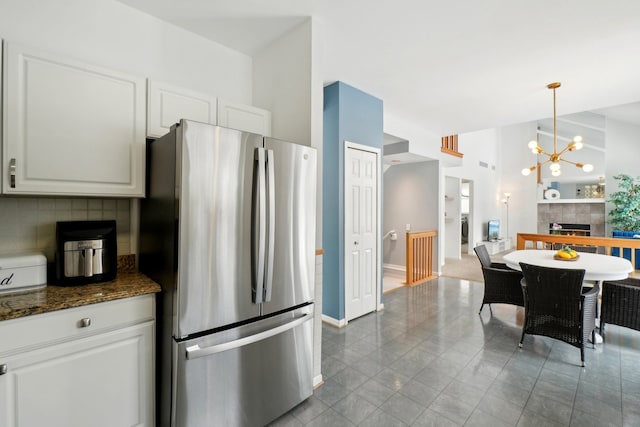 kitchen with a tile fireplace, freestanding refrigerator, hanging light fixtures, white cabinetry, and backsplash