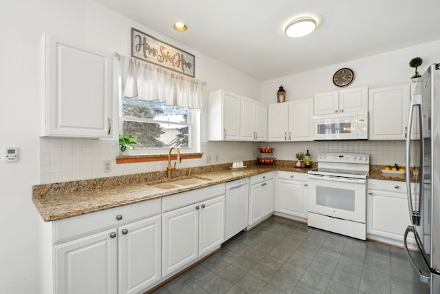 kitchen with backsplash, stone countertops, white cabinets, a sink, and white appliances