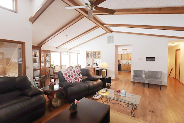 living area featuring visible vents, light wood-style flooring, high vaulted ceiling, beamed ceiling, and ceiling fan with notable chandelier