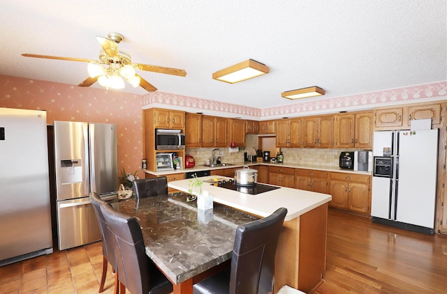 kitchen with a breakfast bar area, appliances with stainless steel finishes, a kitchen island, a sink, and wallpapered walls