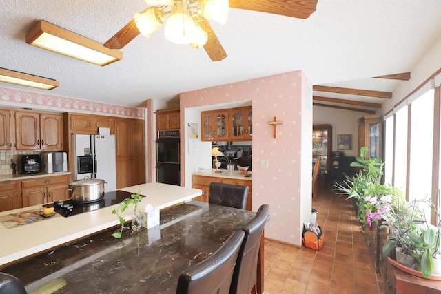 kitchen featuring brown cabinets, a textured ceiling, black appliances, and wallpapered walls