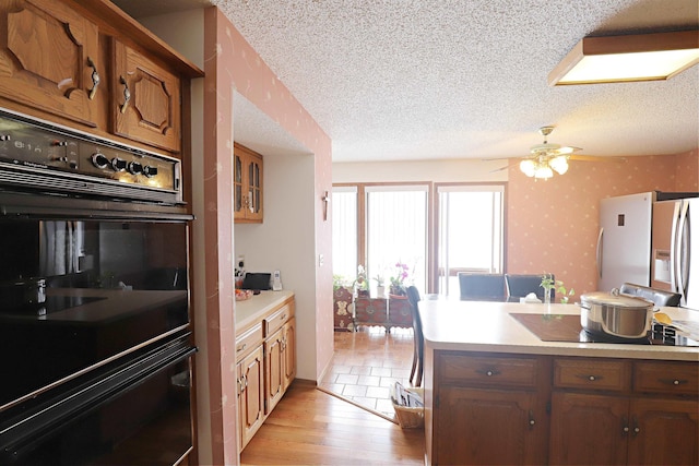 kitchen with a textured ceiling, light countertops, brown cabinets, black appliances, and wallpapered walls