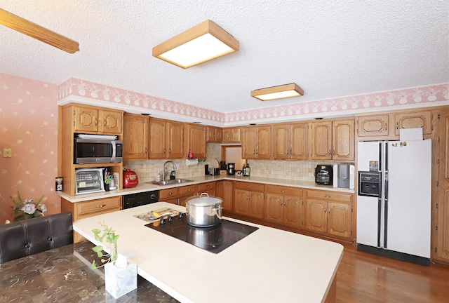 kitchen with dark wood-style floors, light countertops, a sink, black appliances, and wallpapered walls